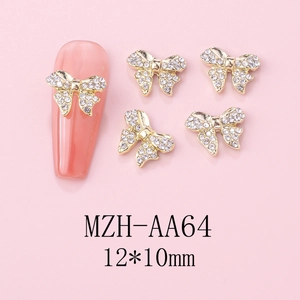 Macro view of gold bow-shaped nail art charms with white crystals on pink background