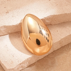 Macro shot of a high-polished golden teardrop brooch resting on natural beige stone