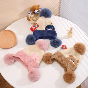 Detail of winter knit hats for kids with plush pom-poms and cute animal embroidery motifs