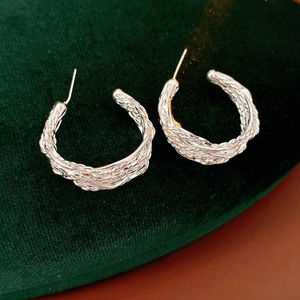 Macro shot of silver plated woven texture hoop earrings on dark velvet surface