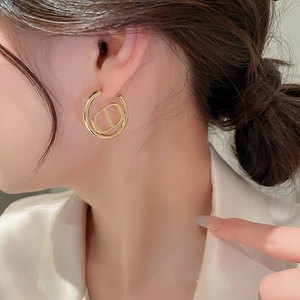 Detail shot of golden double-hoop earrings featuring the iconic CD logo on a model