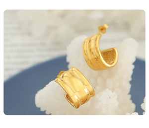 Macro shot of minimalist gold C-shaped hoop earrings resting on white decorative coral