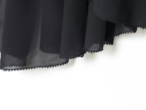 Detailed close-up of black chiffon fabric texture with scalloped hem and professional stitching