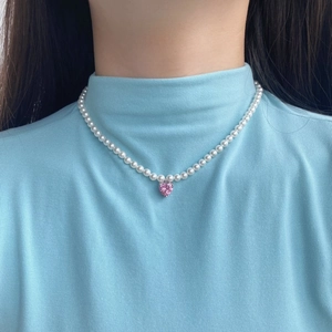 Detail view of the pink heart crystal pendant on a white pearl necklace on model