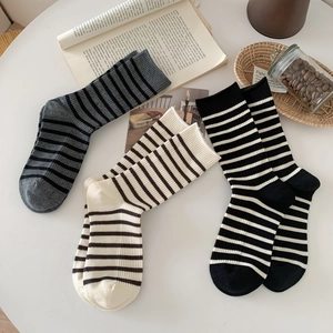 Three pairs of striped cotton crew socks in grey, beige, and black on a minimalist desk