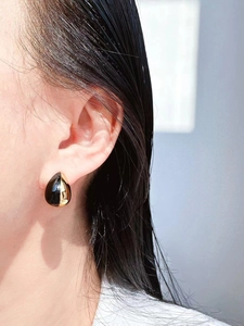 Close-up of a model wearing black and gold teardrop enamel earrings on her ear