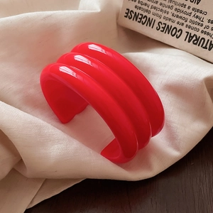 Close-up of bold red resin open bangle with triple parallel stripe texture on beige fabric