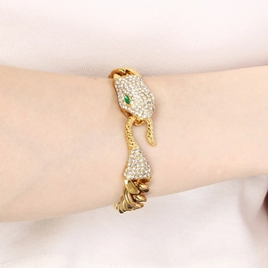 Close-up of gold-plated snake head bracelet with white crystals and green stone eyes
