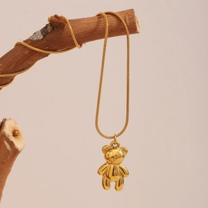 Detailed view of 18K gold plated bear pendant on a thin snake chain over a wood branch