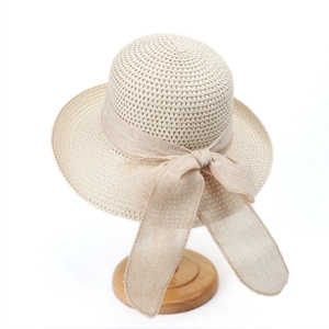 Elegant beige straw sun hat with large bow detail on a stylish wooden stand