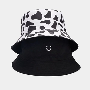 Close-up of a black smiley face bucket hat and a cow print pattern sun hat stacked together
