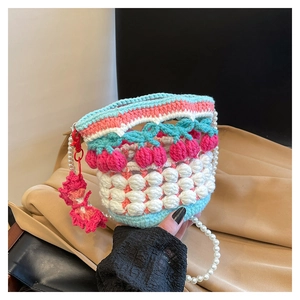 Close-up of knit cherry bucket bag with pearl strap and pink flower charm detail