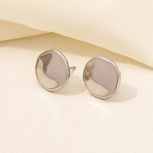 Detailed view of silver irregular round stud earrings on a beige textured fabric background