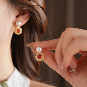Détail de boucles d'oreilles vintage dorées avec pierre rouge, zircons et perle blanche