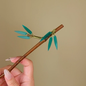 Detail of bamboo joint hairpin with green leaves on hand-held dark brown wooden body