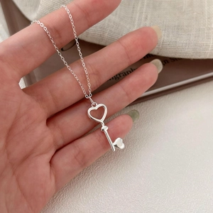 Close-up of polished 925 silver heart key pendant held by hand on a textured background