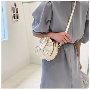Detail of round straw bag featuring floral embroidery and adjustable leather strap