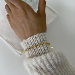 Detail of minimalist 925 sterling silver golden bead bracelet on a soft mohair sweater
