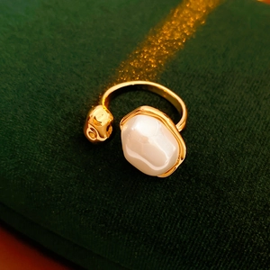Macro d'une bague ouverte dorée avec des perles blanches sur un fond en velours vert