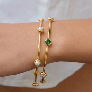 Bracciali in acciaio dorato con perle e zirconi verdi indossati da una modella
