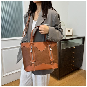 Detail of caramel brown tote bag showing textured leather stitching and silver zippers