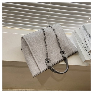 Detailed view of gray tweed tote bag with metal chain strap on a white table
