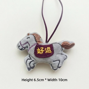Detailed view of plush grey horse charm with purple saddle and golden Good Luck embroidery