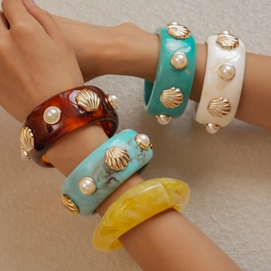 Detailed view of wide resin bangles with gold shell accents and embedded pearls