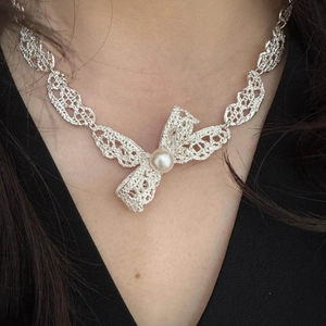 Détail du collier noeud argenté avec perle sur un mannequin pour un look élégant et raffiné
