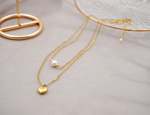 Detail of layered gold titanium necklace featuring freshwater pearl and heart pendant