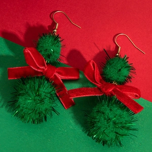 Close-up of Christmas earrings with green pompom, red velvet bow, and golden hooks