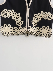 Détail de broderie florale et dentelle sur un haut noir sans manches à boutons