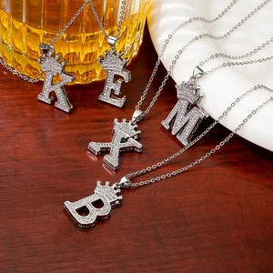 Silver crown initial necklaces with crystal pendants on a dark wood background