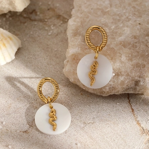 Detail of white shell earring with golden snake pendant on a textured stone background