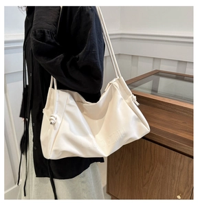 Close-up of cream leather shoulder bag with embossed logo and knotted strap detail