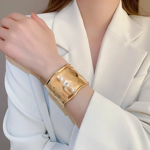 Detail of wide metallic gold bangle featuring a modern textured hammered wave design
