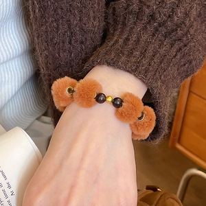 Détail d'un bracelet d'automne avec pompons orange et perles noires sur pull en maille