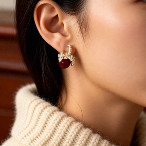 Detail of 18k gold plated earring with deep red pearl and zircon bow-knot on model