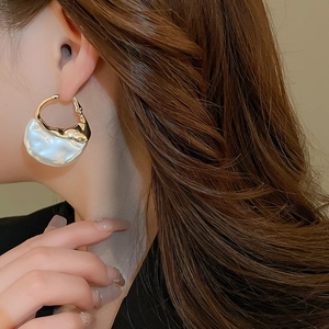 Close-up of elegant gold metal and irregular pearl earring on model ear in French style