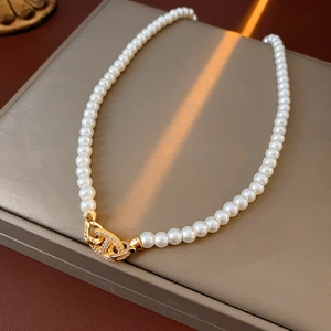 Close-up of white pearl necklace with golden zircon clasp on elegant gray display case