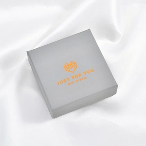 Detailed top view of grey jewelry gift box with gold logo on white silk fabric