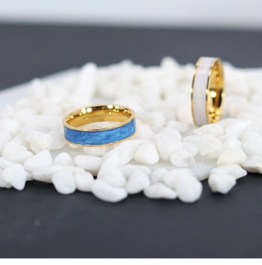 Detail view of blue and white enamel gold-plated rings displayed on white pebbles