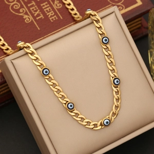 Close-up of gold stainless steel necklace featuring blue evil eye beads on a beige box