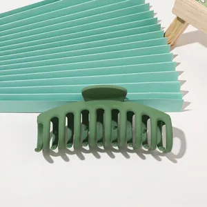 Detail of dark green matte shark hair claw clip with rounded teeth on textured background