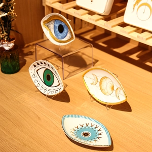 Macro detail of ceramic eye-shaped jewelry trays with golden edges on a wooden stand