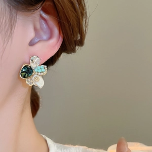 Gros plan de boucles d'oreilles fleurs asymétriques avec gemmes vertes et perles