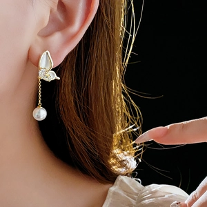 Detailed view of 14K gold plated butterfly tassel earring with white pearl drop on model