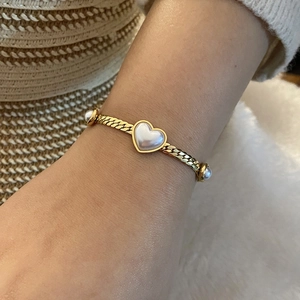 Golden woven bracelet with mother-of-pearl heart pendant and pearl accents worn on wrist