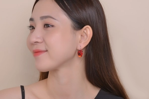 Elegant woman wearing silver earrings with a vibrant red oval gemstone on a neutral background