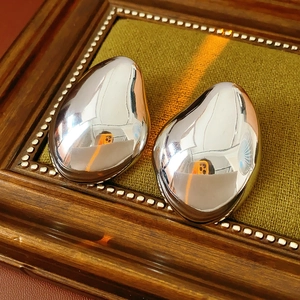Detailed close-up of shiny silver irregular teardrop earrings on green velvet